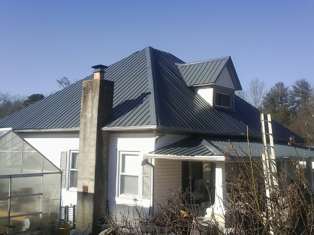 Dark blue standing seam metal roof on a white farmhouse with dormer — Slate & Tile Roof Repair by Roofing Brothers in De Beque
