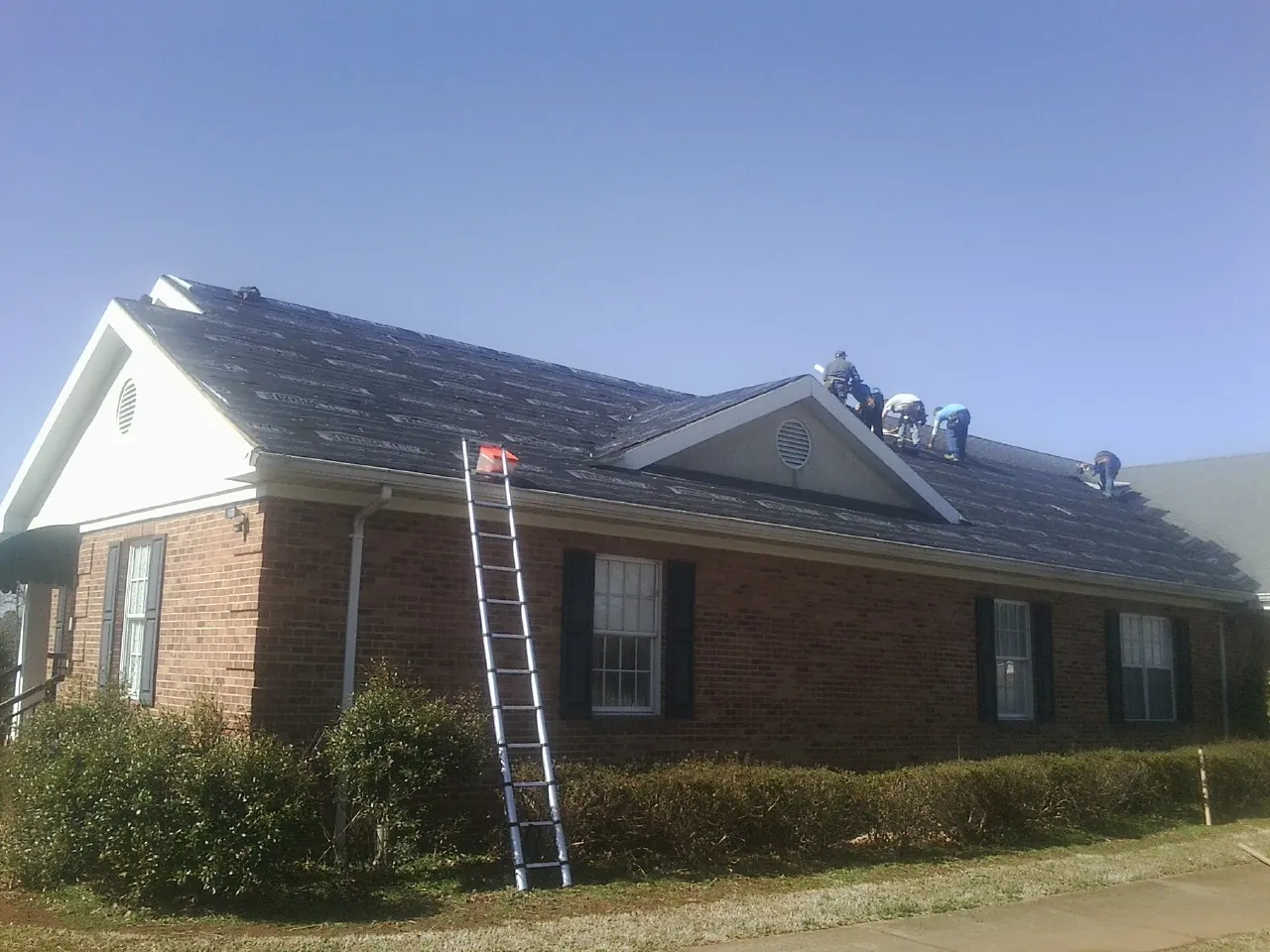 Crew tearing shingles off a brick ranch roof with a ladder set — Metal Roof Repair work by our crew in De Beque
