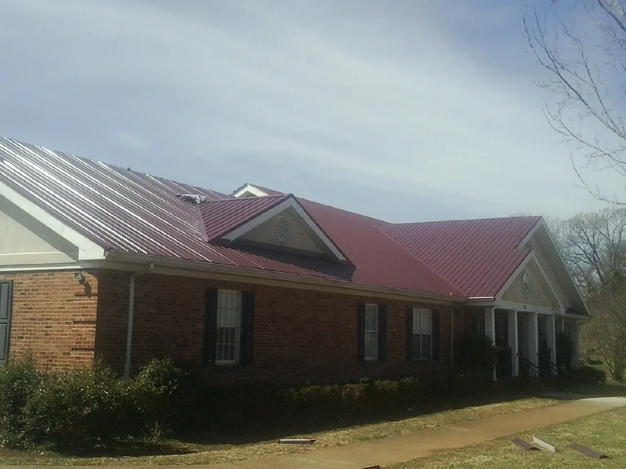 Red metal roof with gabled entries on a long brick building, from a Hail Damage Roof Repair job in De Beque