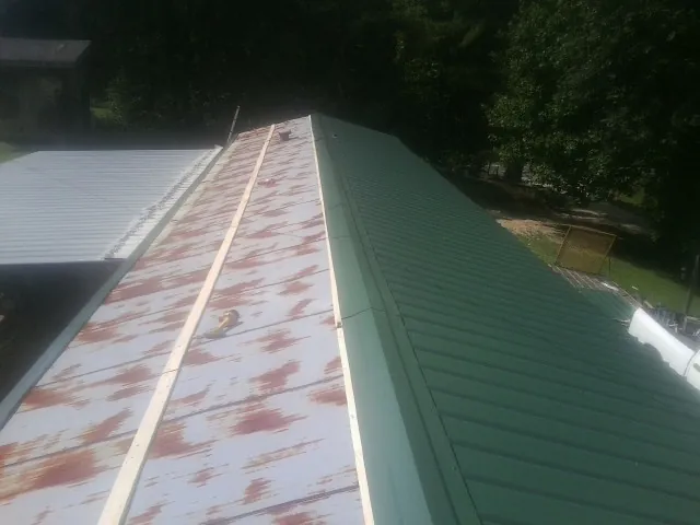 Old rusted panels beside newly installed green metal roofing — Wind Damage Roof Repair by Roofing Brothers in De Beque