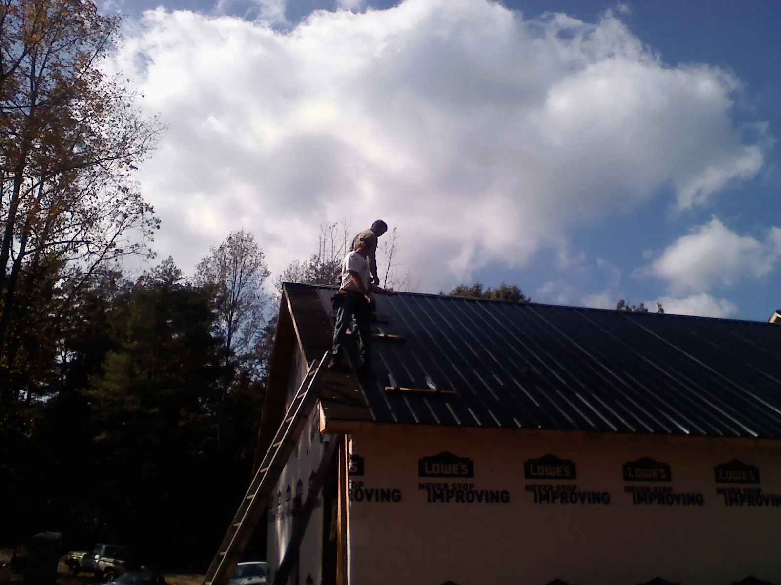Roofer fastening dark metal panels high against a cloudy sky, from a Roof Inspection job in De Beque