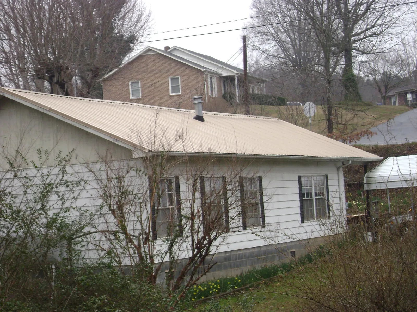 Tan metal roof on a white sided house set into a hillside — Commercial Roofing by Roofing Brothers in De Beque